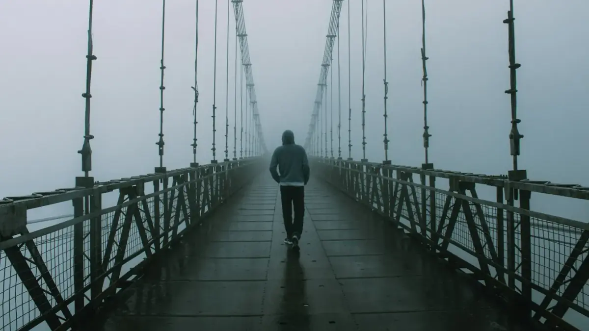 Man walks alone on a foggy suspension bridge.
