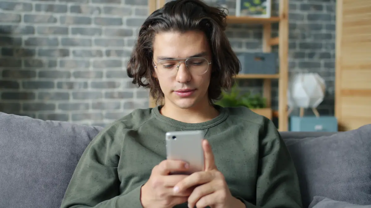 Young man with glasses using a smartphone on couch