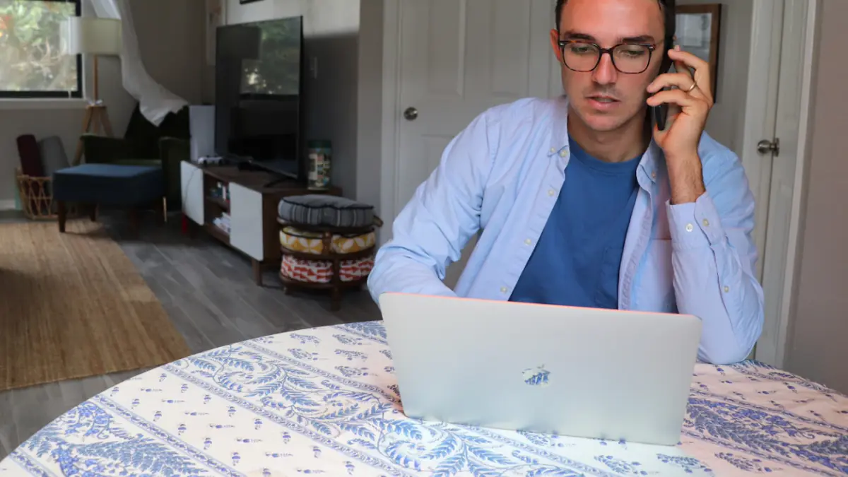 man in white dress shirt wearing eyeglasses sitting by the table using macbook