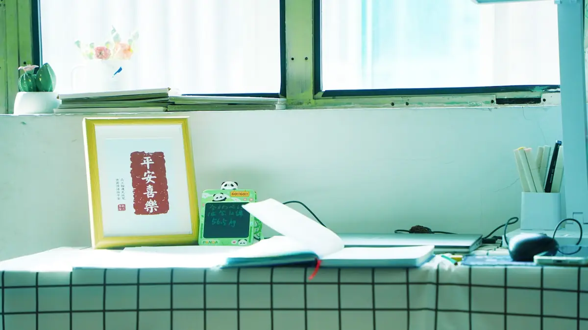 A desk with a framed print, a notebook, and stationery by a window